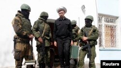 Seorang pejabat angkatan laut Ukraina (tengah) melewati beberapa pria berseragam dan bersenjata, yang diyakini merupakan tentara Rusia, di Sevastopol (19/3). (Reuters/Vasily Fedosenko)