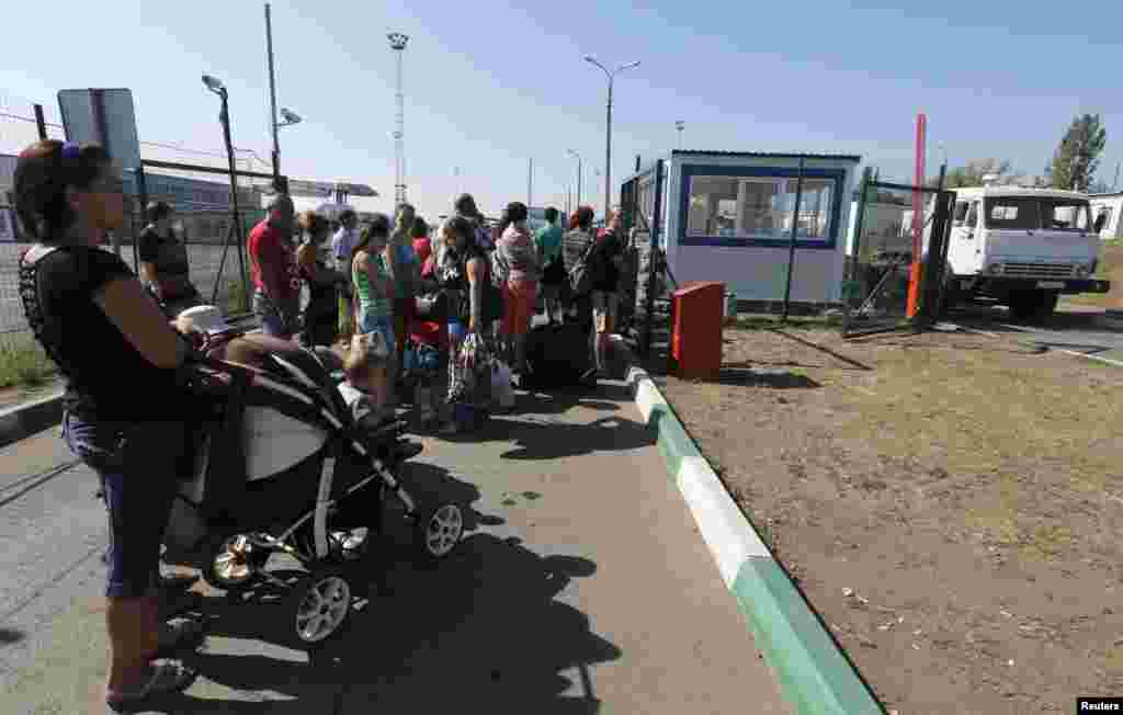 People stand in line to cross the border onto Ukrainian territory as a truck from a convoy that delivered humanitarian aid for Ukraine moves back to Russia at border crossing point "Donetsk" in Russia's Rostov Region, Aug. 23, 2014. 