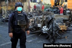 Seorang anggota Densus 88 berdiri di dekat bangkai mobil yang menabrak gereja di Gereja Pentakosta Surabaya Pusat (GPPS), Surabaya, 13 Mei 2018. (Foto: REUTERS/Beawiharta)