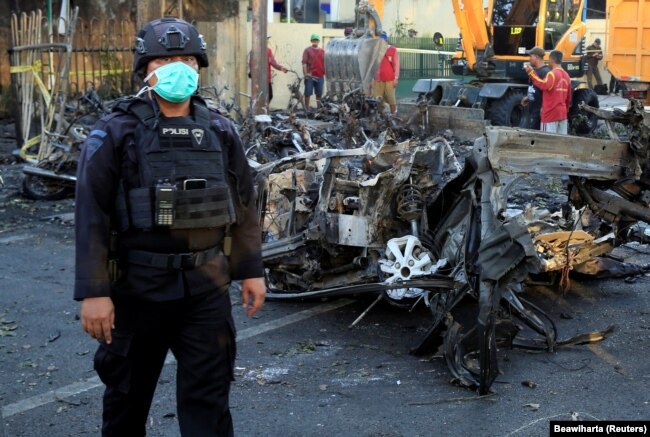 Seorang anggota Densus 88 berdiri di dekat bangkai mobil yang menabrak gereja di Gereja Pentakosta Surabaya Pusat (GPPS), Surabaya, 13 Mei 2018. (Foto: REUTERS/Beawiharta)