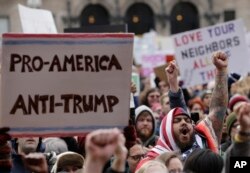 Izzy Berdan, of Boston, center right, wears an American flags as he raises his arm and chants slogans with other demonstrators during a rally against President Donald Trump's order that restricts travel to the US, Jan. 29, 2017, in Boston.