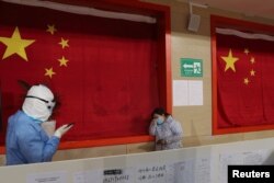 A medical worker in protective suit comforts a patient inside a sports stadium which has been converted into a makeshift hospital to treat patients of the novel coronavirus, in Wuhan, Hubei province, China February 27, 2020.