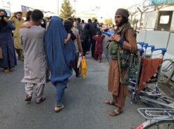 Anggota Taliban berjaga saat orang-orang berjalan di pintu masuk Bandara Internasional Hamid Karzai di Kabul, Afghanistan, 16 Agustus 2021. (REUTERS/Stringer)