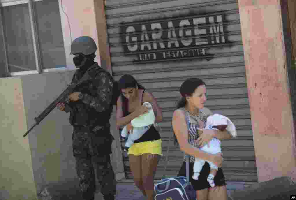 Women carring their babies walk past a soldier during an operation at the Rocinha slum, in Rio de Janeiro, Brazil. More than 1,000 police and soldiers are searching Rio&#39;s largest slum for weapons and ammunition amid a crackdown on drug gangs.