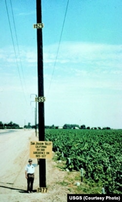 Historic 1977 photo depicting the location of maximum land subsidence in the U.S., near Mendota, CA in the San Joaquin Valley. Joseph Poland (pictured), USGS, scientific subsidence studies pioneer, placed the date signs to indicate previous elevations.