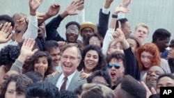 FILE - U.S. President George H.W. Bush is surrounded by cheering students from the Independent Living Program in Los Angeles, as Bush prepared to leave Los Angeles International Airport after presenting a Point of Light award in the area, May 21, 1990. 