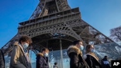 Para pengunjung mengenakan masker untuk melindungi dari penularan COVID-19, melintas di depan Menara Eiffel di Paris, Perancis, 21 Desember 2021. (Foto: Michel Euler/AP Photo)