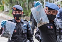 Polisi anggota regu penjinak bom, menunjukkan kantong plastik berisi barang-barang yang dikumpulkan di dekat lokasi ledakan hari Minggu di Katedral Hati Kudus Yesus, termasuk apa yang diyakini sebagai bagian dari alat peledak yang digunakan dalam serangan bom bunuh diri di Makassar, Sulawesi Selatan, Senin, 29 Maret 2021. (AP Photo / Yusuf Wahil)