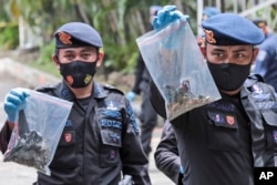 Polisi anggota regu penjinak bom, menunjukkan kantong plastik berisi barang-barang yang dikumpulkan di dekat lokasi ledakan hari Minggu di Katedral Hati Kudus Yesus, termasuk apa yang diyakini sebagai bagian dari alat peledak yang digunakan dalam serangan bom bunuh diri di Makassar, Sulawesi Selatan, Senin, 29 Maret 2021. (AP Photo / Yusuf Wahil)