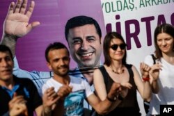 In this photo taken June 5, 2018, people dance in front of an election campaign poster of Selahattin Demirtas, Turkey's jailed pro-Kurdish politician and presidential candidate, in Istanbul.