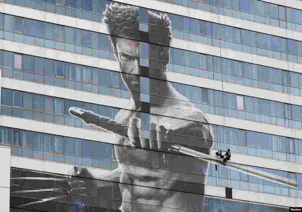 A worker installs a poster of Hugh Jackman&#39;s new movie &quot;The Wolverine&quot; on a building in Bangkok, Thailand.