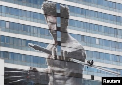 FILE - A worker installs a poster of Hugh Jackman in the new movie "The Wolverine" on a building in Bangkok July 9, 2013.