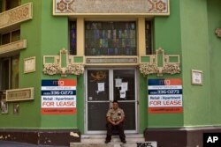 A private security guard sits in front of a closed down business in the colonial district of Old San Juan, Puerto Rico, Sunday, Aug. 2, 2015.