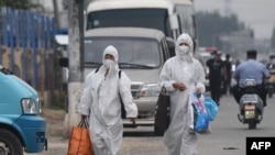 Two women wear protective suits as they walk on a street near the closed Xinfadi market in Beijing on June 13, 2020.