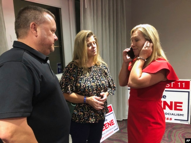 Supporters stand with construction executive Marjorie Taylor Greene, right, as she's on the phone, late Tuesday, Aug. 11, 2020, in Rome, Ga.