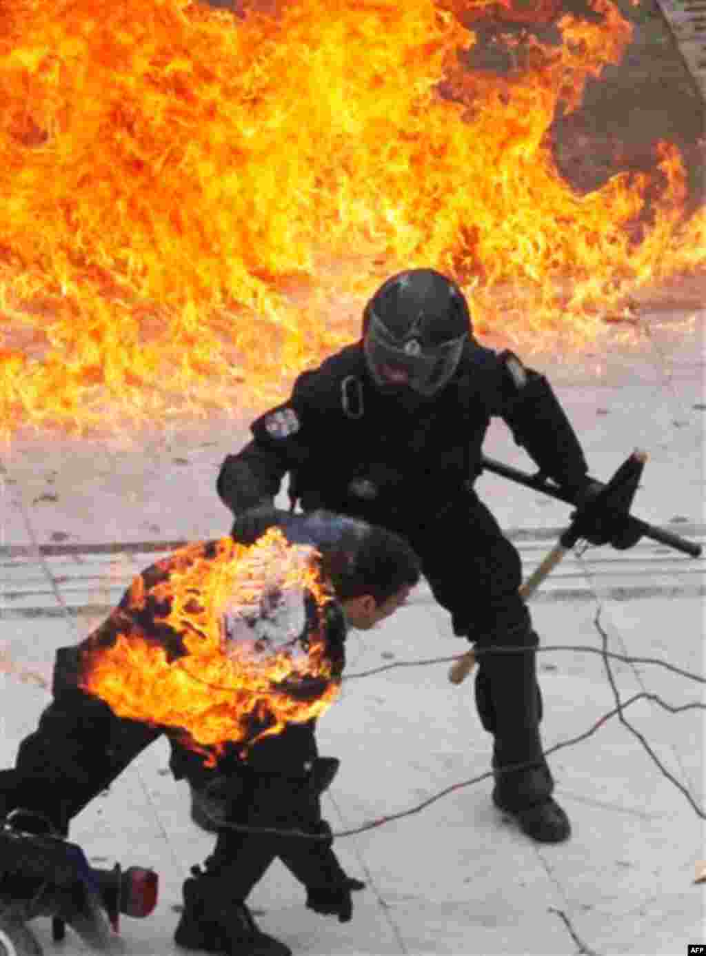 A motorcycle policeman burns, front, as his colleague tries to help him after protesters threw a petrol bomb in Athens. Scores of youths hurled rocks and petrol bombs at riot police after clashes broke out Wednesday during a mass rally taking place as par