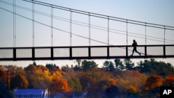 A jogger crosses the Swinging Bridge over the Androscoggin River on a frosty autumn morning, Nov. 4, 2021, in Brunswick, Maine. 