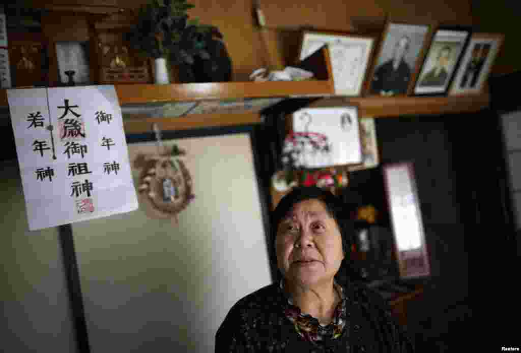 Kimiko Koyama, who evacuated from Miyakoji three years ago, looks up inside her house with portraits of her deceased parents in the background, Tamura, Fukushima prefecture, April 1, 2014.