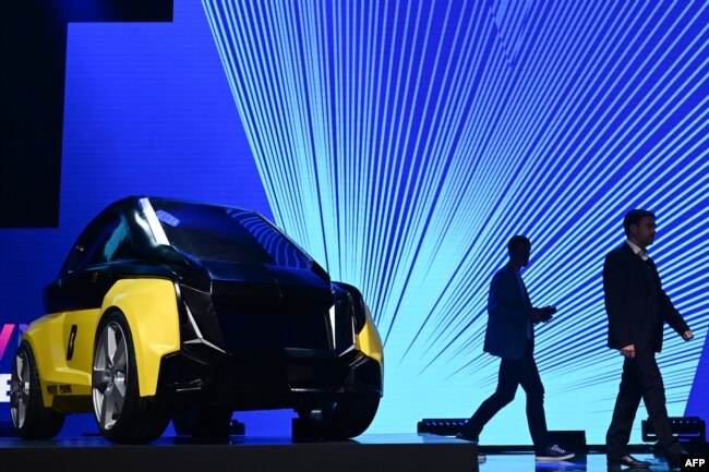 Two men walk past a prototype of an electric car made by the Bolt Mobility company, displayed at the Viva Tech startups and innovation fair, in Paris, May 16, 2019.