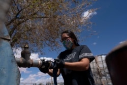 Raynelle Hoskie attaches a hose to a water pump to fill tanks in her truck outside a tribal office on the Navajo reservation in Tuba City, Ariz., on April 20, 2020.