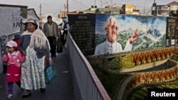 Residentes de El Alto, Bolivia, caminan frente a un mural alusivo a la visita del Papa a Ecuador, Bolivia y Paraguay.