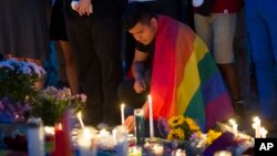 Seorang pria berselimut bendera pelangi menyalakan lilin dalam doa bersama di Washington (13/6).