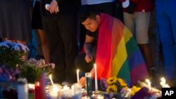 An unidentified man, wrapped in a rainbow flag, lights a candle during a vigil in Washington, June 13, 2016.