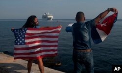 FILE - Yaney Cajigal, left, and Dalwin Valdes hold up U.S. and Cuban flags as they watch the arrival of Carnival's Adonia cruise ship from Miami, in Havana, Cuba, May 2, 2016.