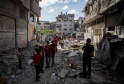 Warga Palestina berjalan di tengah puing-puing rumah yang hancur terkena serangan udara Israel dini hari, di Kota Gaza, Senin, 17 Mei 2021. (AP Photo / Khalil Hamra)