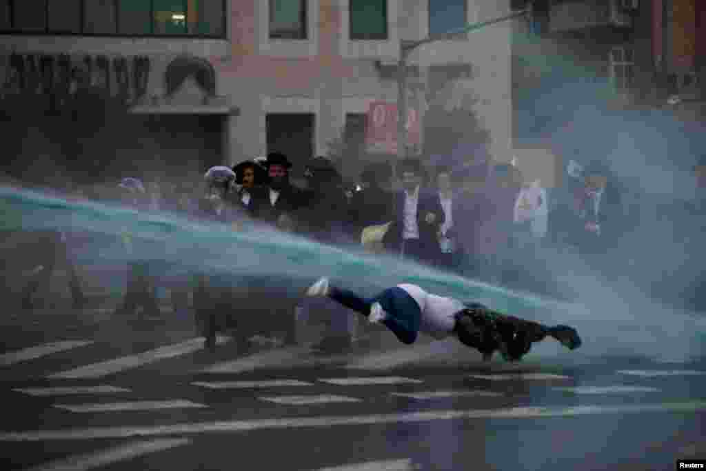 A bystander falls as Israeli police spray water during a demonstration by ultra-Orthodox Jews against the detention of members of their community who failed to report to a military recruiting office, in Jerusalem.