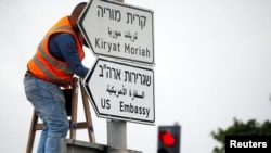 FILE - A worker hangs a road sign that directs traffic to the U.S. Embassy, in the area of the U.S. Consulate in Jerusalem, May 7, 2018.