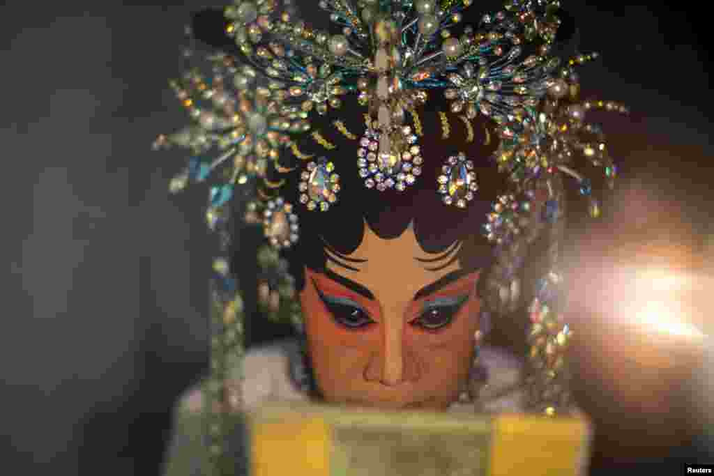A member of a Chinese opera troupe looks on as she applies make-up before performing at a shrine during the annual vegetarian festival in Bangkok, Thailand.