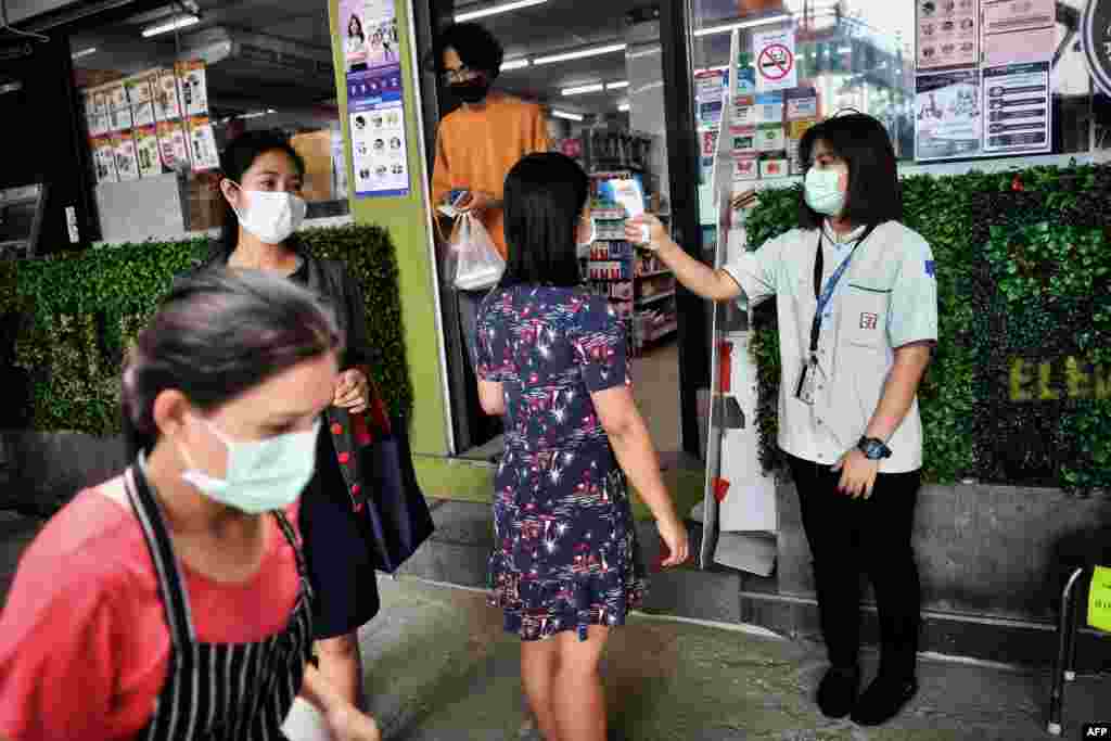 A 7-11 convenience store employee takes the temperature of a customer before allowing her to enter, in an effort to contain the spread of the COVID-19 coronavirus, in Bangkok.