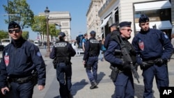 Police officers and riot police officers, right, patrol on the Champs Elysees boulevard in Paris, April 21, 2017. 