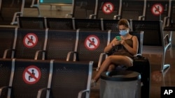 In this June 30, 2020, file photo, a passenger sits at Barcelona airport in Barcelona, Spain. (AP Photo/Emilio Morenatti)