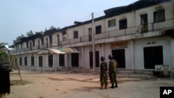 In this photo taken with a mobile phone, soldiers stand outside a burnt out shopping mall in Maiduguri, Nigeria, Monday, Oct. 8, 2012.