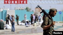 FILE - A Kurdish People's Protection Units (YPG) fighter walks near residents who had fled Tel Abyad, as they re-enter Syria from Turkey after the YPG took control of the area, at Tel Abyad town, Raqqa governorate, Syria, June 23, 2015. 