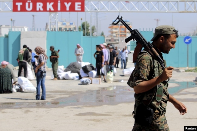 FILE - A Kurdish People's Protection Units (YPG) fighter walks near residents who had fled Tel Abyad, as they re-enter Syria from Turkey after the YPG took control of the area, at Tel Abyad town, Raqqa governorate, Syria, June 23, 2015.