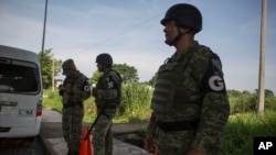 La policía militar que lleva la insignia de la nueva Guardia Nacional proporciona seguridad perimetral mientras un agente de migración espera para revisar los documentos de los pasajeros que pasan por el transporte, en un puesto de control de inmigración, al sur de México.