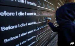 FILE - A girl writes on a chalkboard outside the Art on Sedgwick storefront studio in Chicago, Oct. 18, 2015. The chalkboard was installed to get people interacting on a street where few people stop to chat.