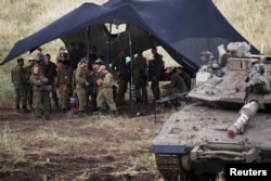 Israeli soldiers stand in the shade next to a tank near the Israeli side of the border with Syria in the Israeli-occupied Golan Heights, May 9, 2018.