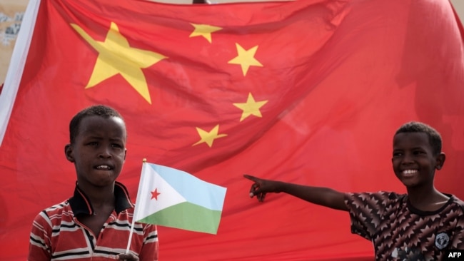 在中国资助的有千所住房单位的吉布提建筑工程启动仪式之前,拿着吉布提国旗的小男孩站在巨大的中国国旗前。(2018年7月4日)