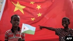 FILE - A boy holds the Djiboutian national flag in front of the Chinese national flag as he waits for Djibouti’s president, Ismaïl Omar Guelleh, before the launching ceremony of a China-financed 1,000-unit housing construction project in Djibouti, July 4, 2018.