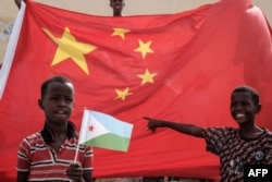 FILE - A boy holds the Djiboutian national flag in front of the Chinese national flag as he waits for Djibouti's President Ismail Omar Guellehas before the launching ceremony of China-financed 1,000-unit housing construction project in Djibouti, July 4, 2018.