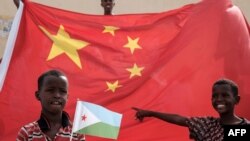 一名手舉吉布提國旗的男孩站在中國國旗前等待參加中國資助的住房建設項目啟動儀式（法新社2018年7月4日）