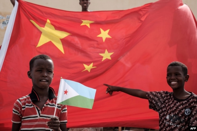 FILE - A boy holds the Djiboutian national flag in front of the Chinese national flag as he waits for Djibouti's President Ismail Omar Guellehas before the launching ceremony of China-financed 1,000-unit housing construction project in Djibouti, July 4, 2018.