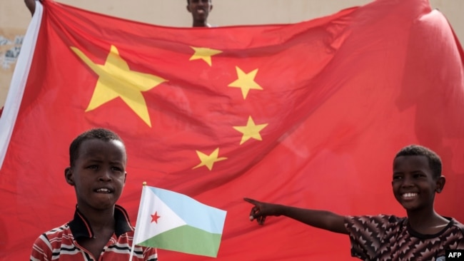 一名手举吉布提国旗的男孩站在中国国旗前等待参加中国资助的住房建设项目启动仪式（法新社2018年7月4日）