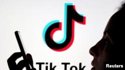 A person holds a smartphone as Tik Tok logo is displayed behind in this picture illustration taken November 7, 2019. Taken 11.7.2019