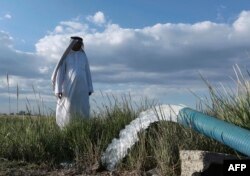 In this April 23, 2019, photo, a farmer stands near a water pump on his farm in Youssifiyah, Iraq. In the farming region, just south of the capital, canals that were empty last year are flush with water.