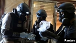 A U.N. chemical weapons expert, wearing a gas mask, holds a plastic bag containing samples from one of the sites of an alleged chemical weapons attack in Ain Tarma neighborhood of Damascus, Syria, Aug. 29, 2013.